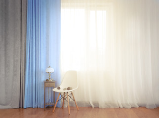 Small table with lamp and chair on curtain background