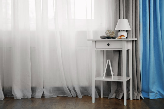Small white table with lamp on curtain background