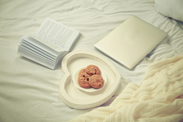Open book, laptop and cookies on a bed