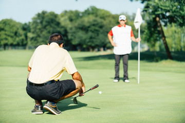 Fototapeta premium Golf game. Golfer reading green, caddy holding flag