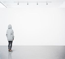 Young woman walking in modern gallery and looking at the blank canvas. Square