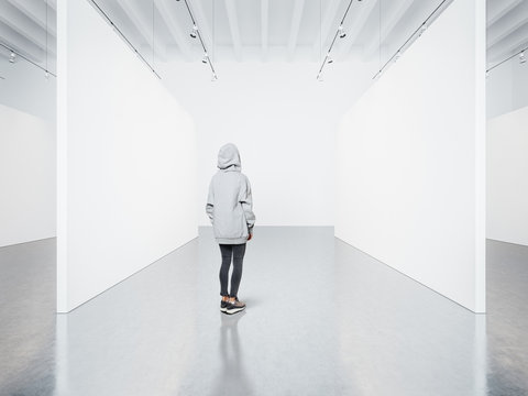 Photo of girl in empty modern gallery looking at the blank canvas. 