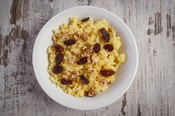 Cooked millet groats with raisins and walnuts on white plate, healthy food and nutrition