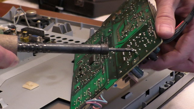 Close up of hands of repair man holding a printed circuit board pcb and soldering iron and removing faulty part of lcd tv.