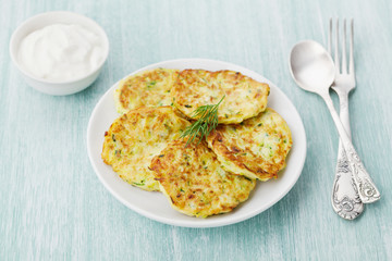 Zucchini cabbage pancakes or vegetable fritters with sour cream on wooden kitchen table