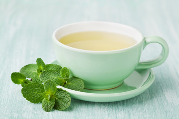 Cup of mint tea and green leaves on light table, useful herbal drink