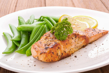 Grilled salmon with lemon, green bean and herb, on white dish. Dinner concept