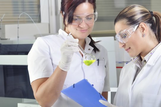 Attractive young PhD student scientist observing the green indicator color shift after the solution destillation in chemical laboratory 
