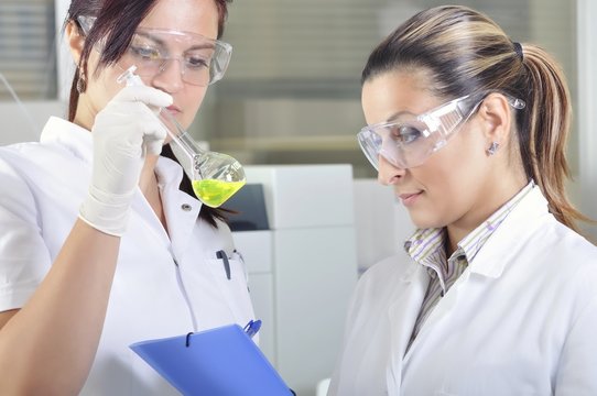 Attractive young PhD student scientist observing the green indicator color shift after the solution destillation in chemical laboratory 
