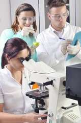 Young scientists studying new substance or virus in microscope