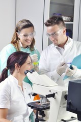 Young scientists studying new substance or virus in microscope