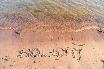happy holidays written in the sandy beach