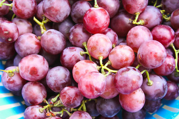 Red grape berries in blue basket on straw tray closeup