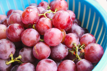 Red grape berries in blue basket on straw tray closeup