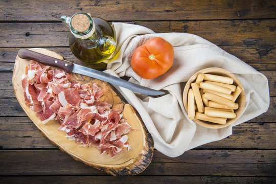Tabla con virutas de jamón serrano cortado a cuchillo con tomate aceite de oliva y picos de pan para un aperitivo y dieta saludables