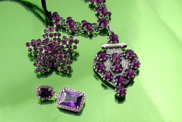 Silver fashion jewelry with purple rhinestones on green mirrorlike background