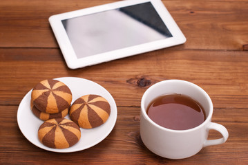 Cup of tea and cookies a digital tablet on the wooden table.