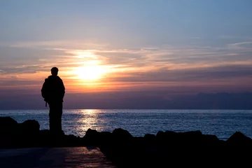 Foto auf Acrylglas Meer / Sonnenuntergang Silhouette of a man admiring winter sunset over italian sea - negative space on the right