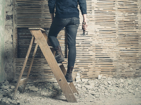 Woman standing on stepladder by wattle and daub wall