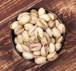 Black bowl of pistachios on aged wooden background