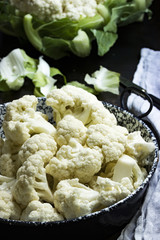 Blumenkohlröschen zum Kochen vorbereitet in einem Topf mit ganzem Blumenkohl im Hintergrund