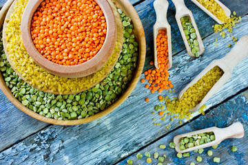 Colorful variety of cereals in a bowls and scoops on wooden background. Red lentils, yellow bulgur and green dried peas