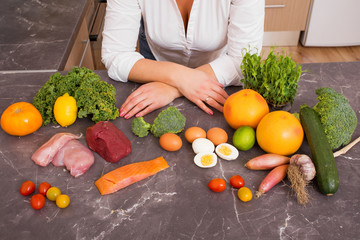 Woman in kitchen with variety of vegetables and raw food 