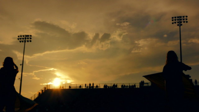 Silhouetted color guard preforming before a high school football game as the sun sets.