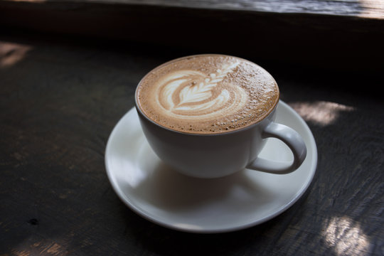 Latte art on cappuccino coffee on dark wood background