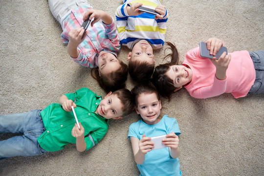happy children with smartphones lying on floor