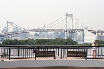 A girl on Odaiba island taking picture of the bridge on a background