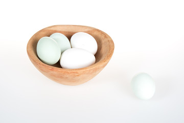 Green and white eggs in a wooden bowl on a white table