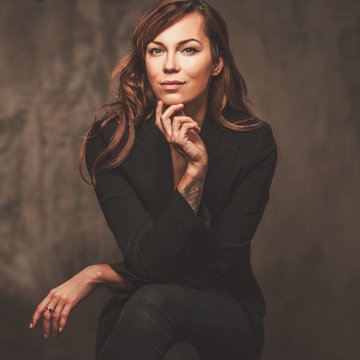 Attractive Beautiful Woman In Black Sitting On Chair Isolated On Gray Background.