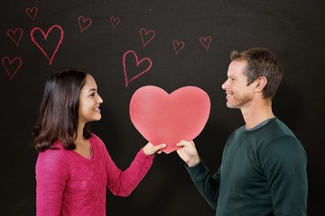 Composite image of smiling couple holding red heart shape 