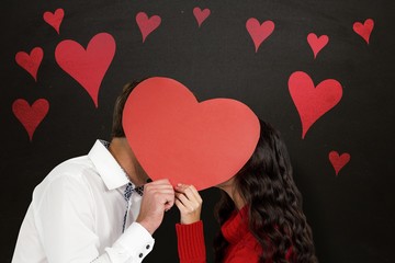 Composite image of couple covering faces with paper heart