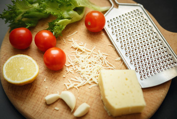 Cheese, tomatoes, garlic with grater on wooden catting board