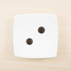 The two dark chocolate buttons and small white square disk on light brown wooden board.