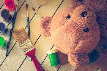 Teddy bear lying on wooden background with tempera paints and paint brushes