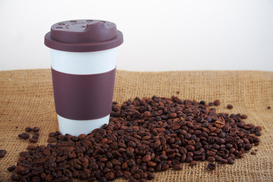 Takeaway ceramic cup and coffee beans on blue background
