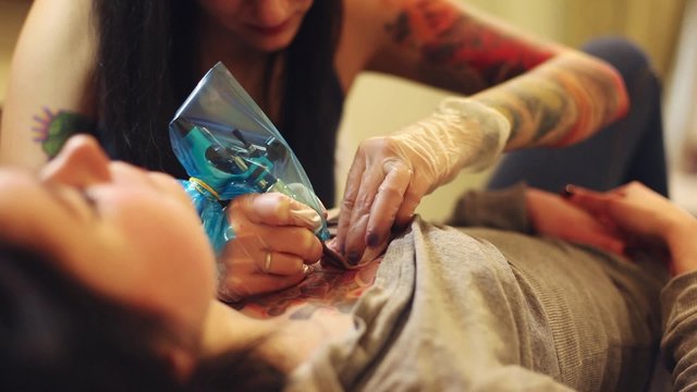 Cinemagraph loop - Young girl tattoo artist working on a tattoo for a girl on her chest - motion photo
