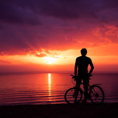Fototapeta na wymiar Man Standing with a Bike at Sunset by the Sea