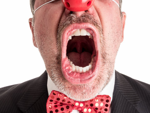 Closeup photograph of a man in a business suit with a red rubber nose and a sparkly red bow tie screaming toward the camera.