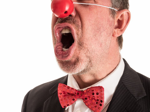 Closeup photograph of a man in a business suit with a red rubber nose and a sparkly red bow tie screaming at the top of his lungs.