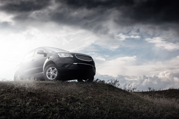 Black car stay on hill in dramatic clouds at daytime
