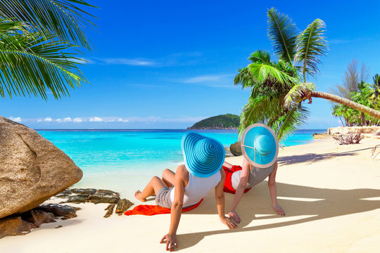 Two women with hats enjoying sun holidays on the tropical beach