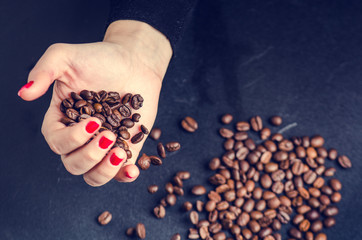    Coffee beans on a black background. Woman´s hand keep a beans. Hot drink. Close up.
   