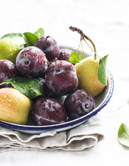 fresh plums and pears on a white enamel plate on a light background