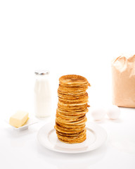 Pile of pancakes with ingredients, on white background.