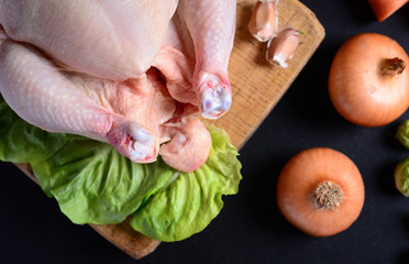 Raw chicken with vegetables on black background