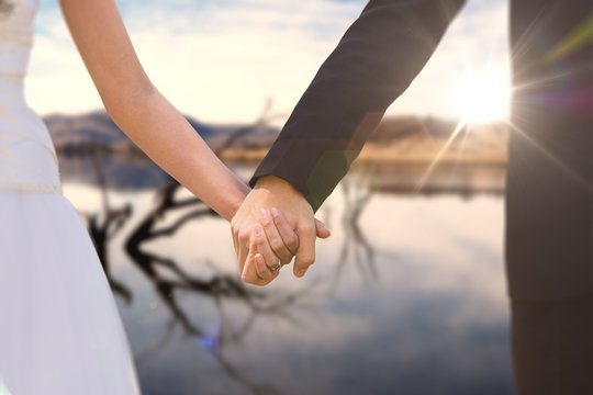 Composite image of mid section of newlywed couple holding hands 